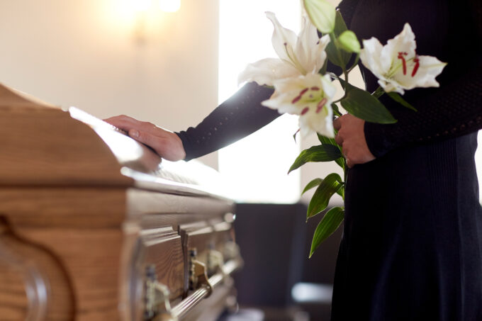 A woman holds flowers and places her hand on a funeral casket