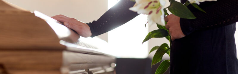 A woman holds flowers and places her hand on a funeral casket